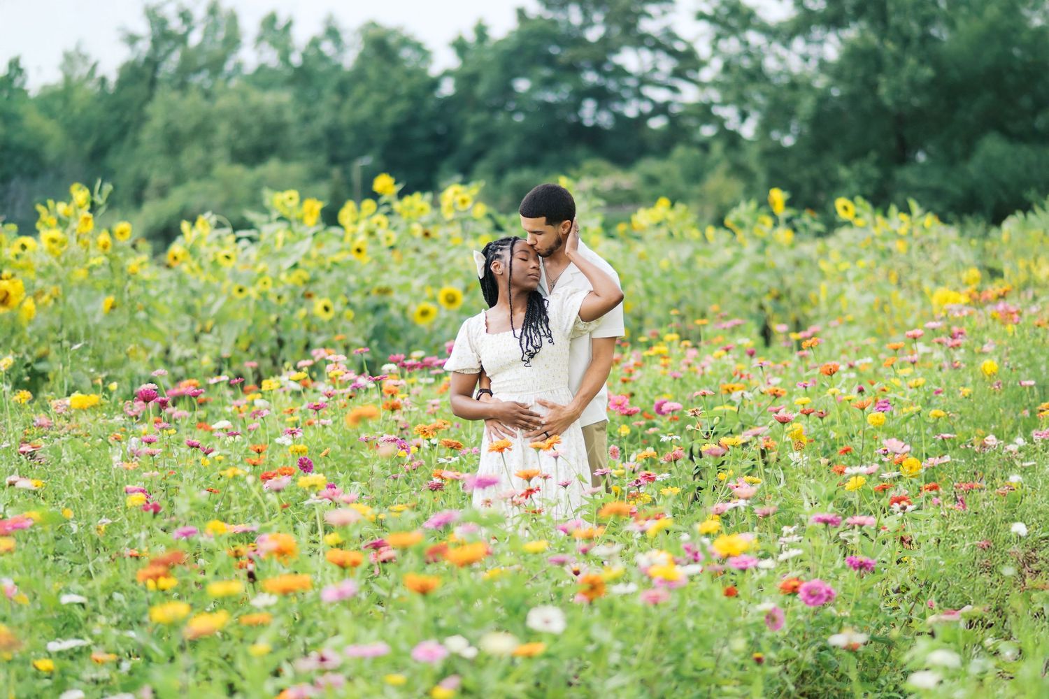 Romantic couple embraces in a vibrant wildflower field filled with yellow and pink blooms on a sunny summer day.