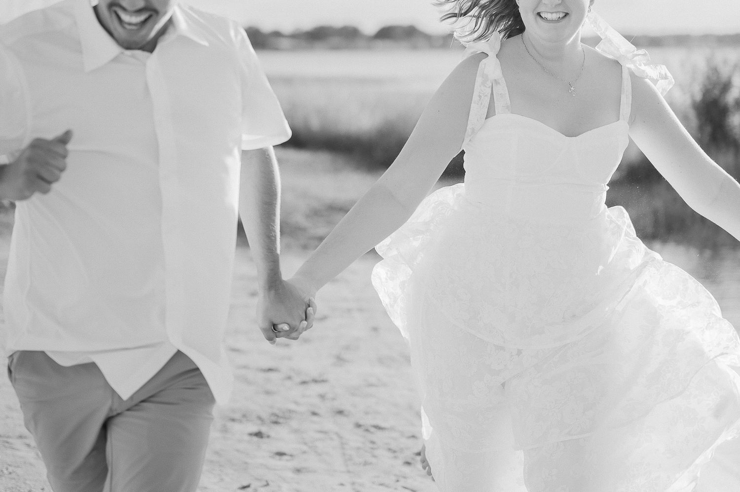 A joyful couple in white wedding attire share a romantic moment on a sunny beach during their seaside celebration.