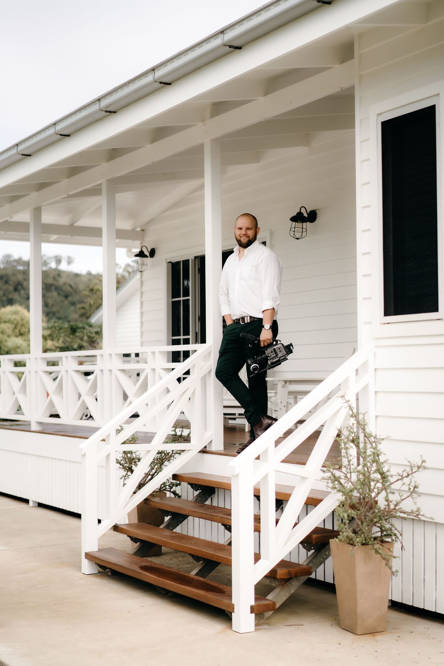 An elegant white veranda with wooden steps featuring cross-rail details and black doors on a modern farmhouse exterior.
