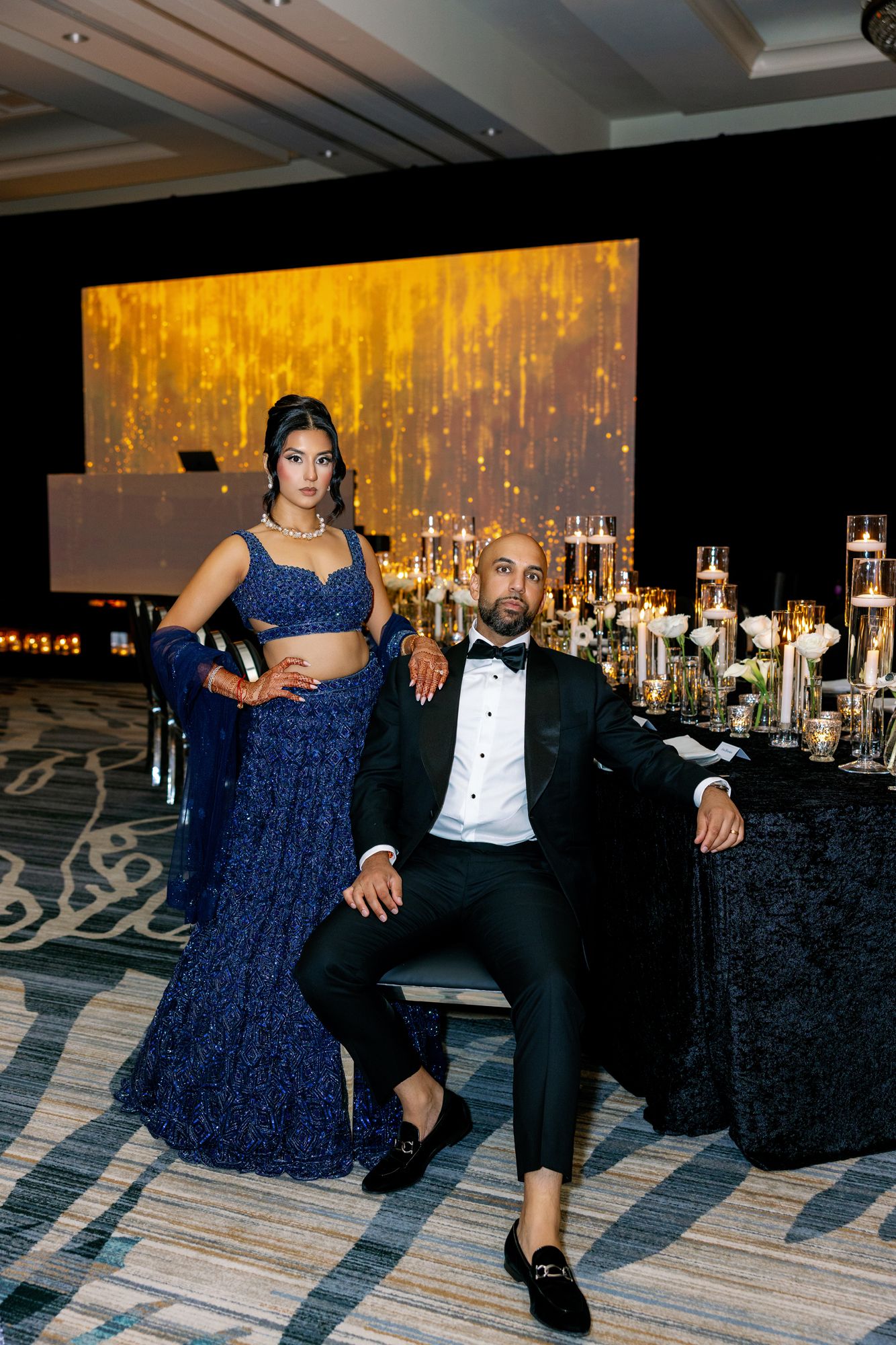 A couple in formal attire dances together at an elegant reception with glowing lights and dark tablecloths in the background.