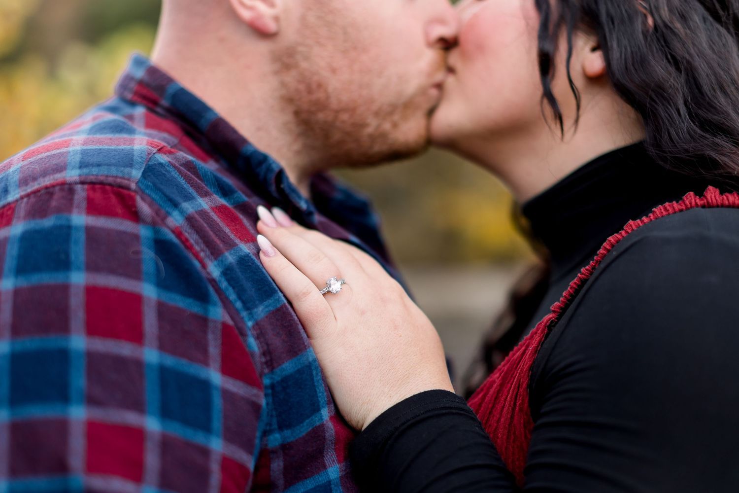 A romantic couple shares a tender kiss in front of a blurred outdoor background.