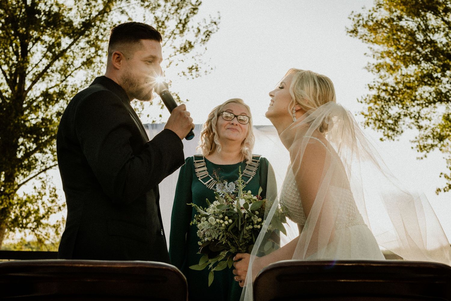 A joyful wedding ceremony moment captured in golden sunlight with a celebrant and couple.