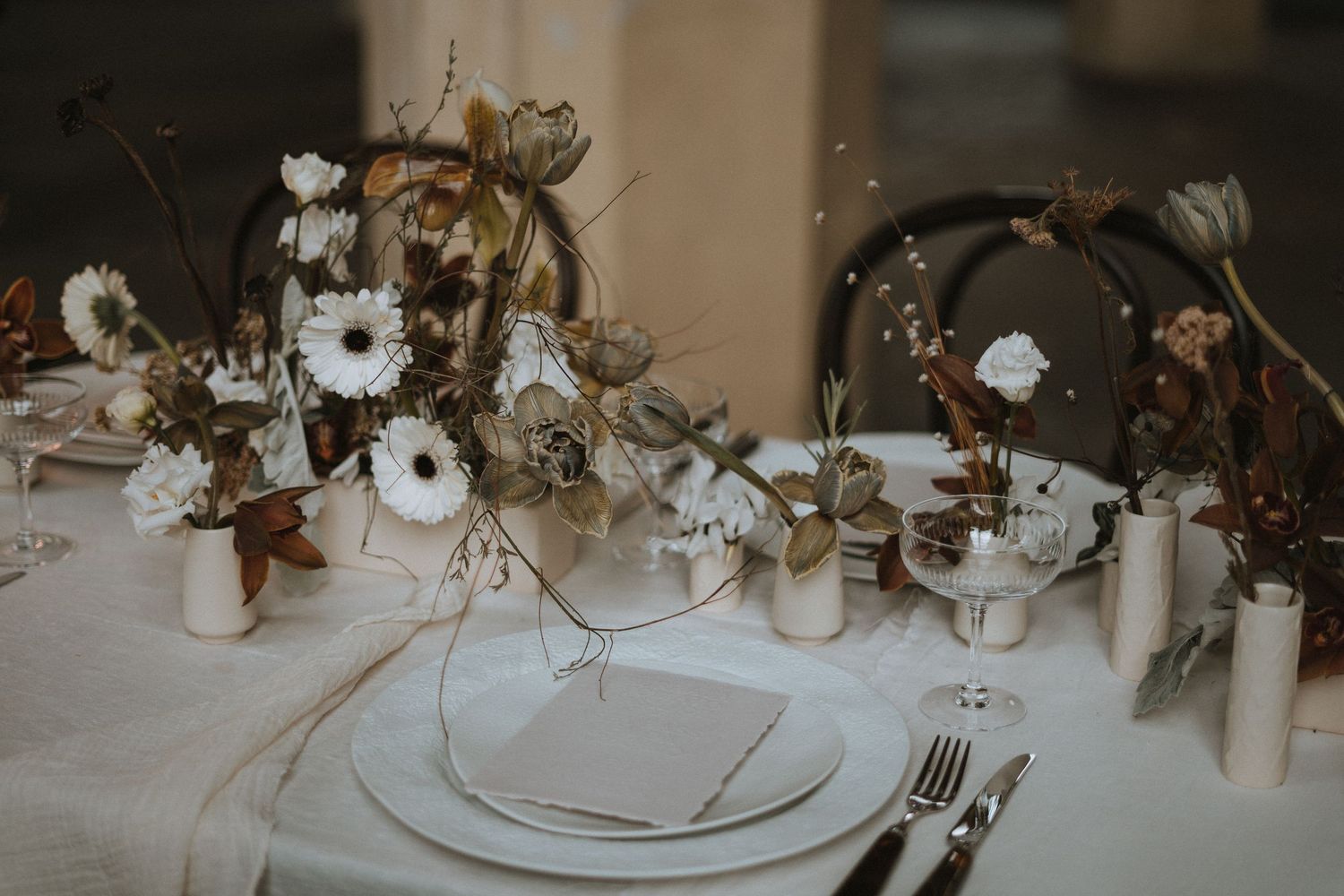 Elegant wedding tablescape with neutral floral arrangements, taper candles, and crystal glassware on white linens.