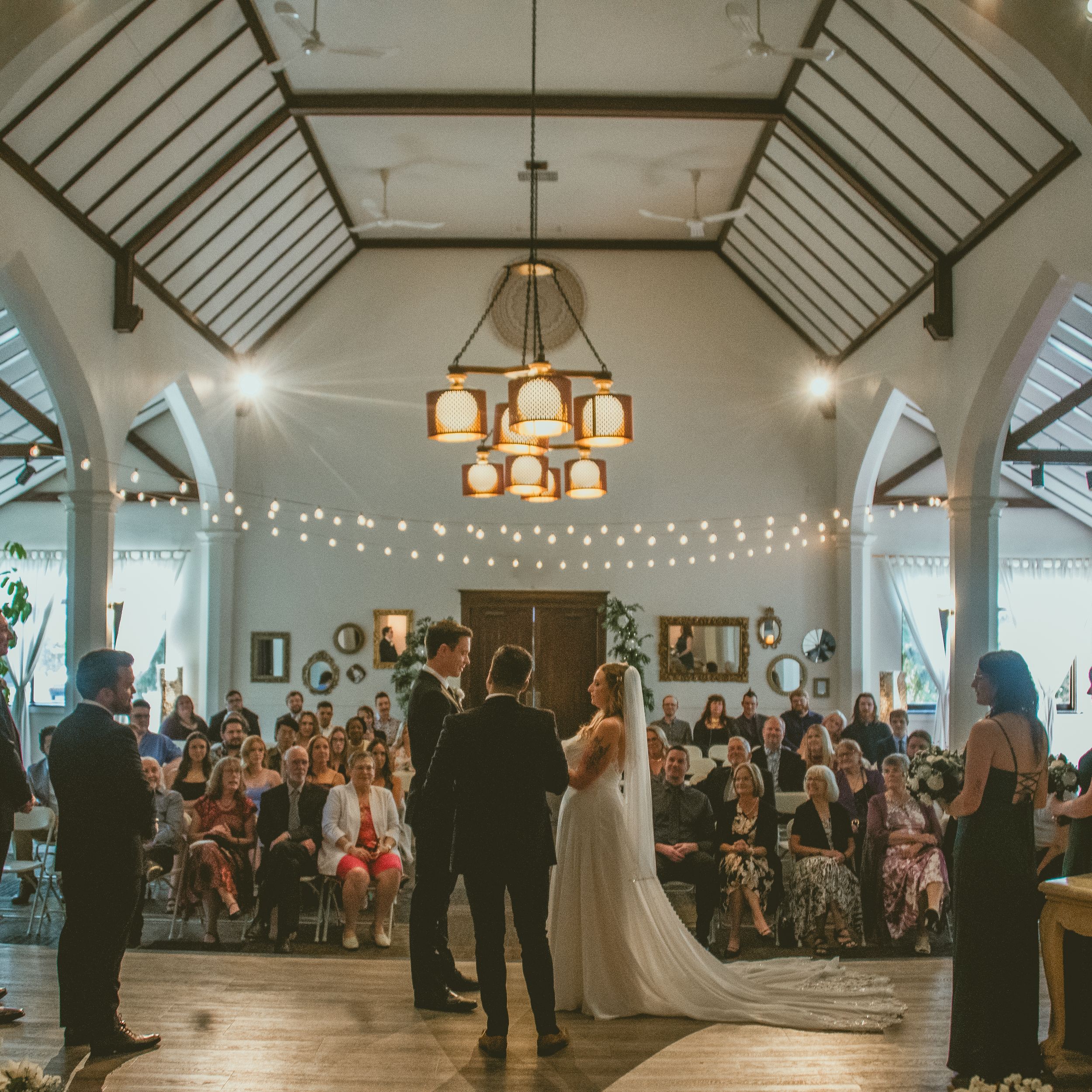 Wedding guests watch as newlyweds share their vows under string lights in Studio 96 Edmonton Wedding Photographer