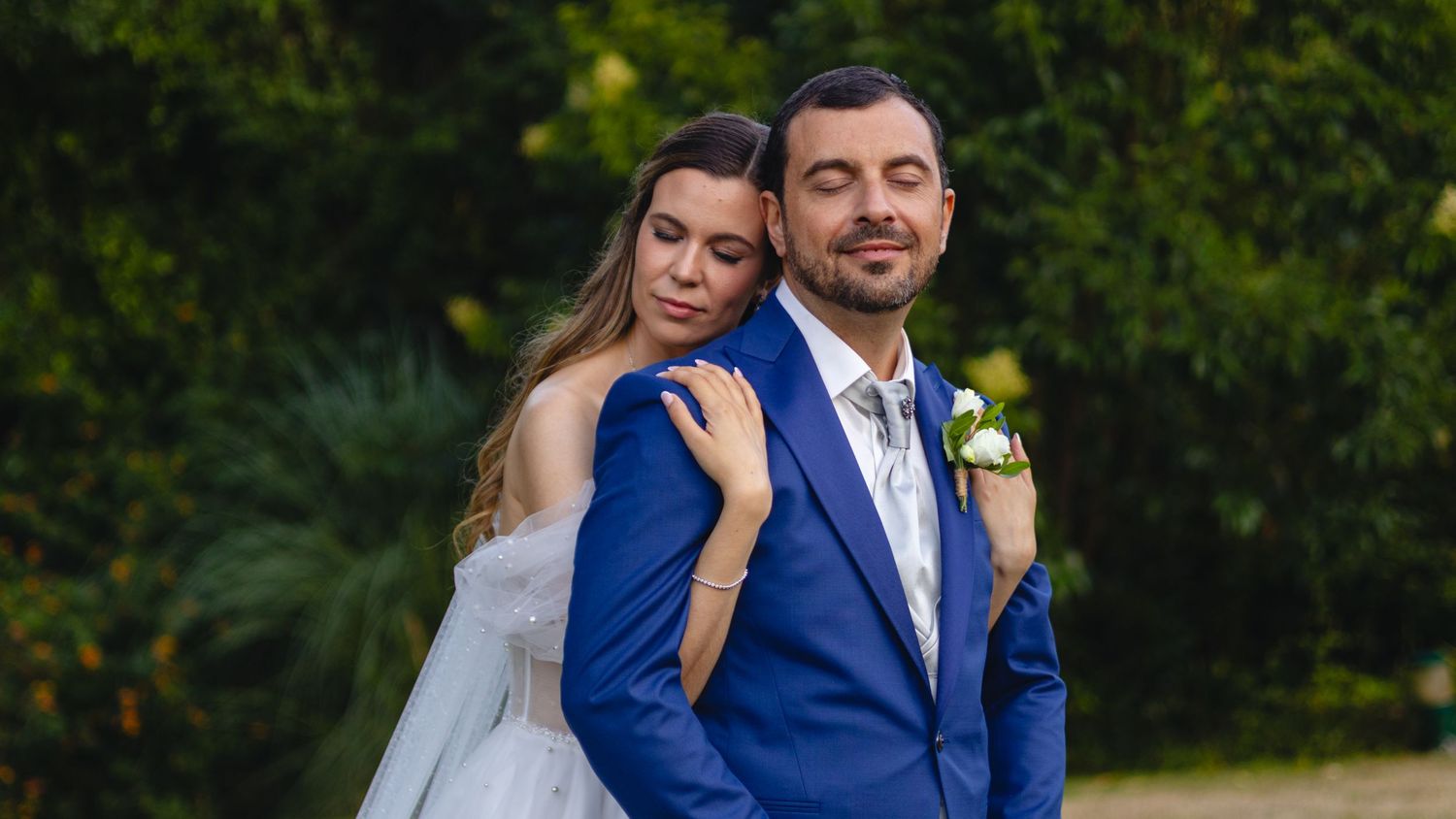 Bride and groom share intimate moments in a garden setting while wearing blue suit and white wedding dress.