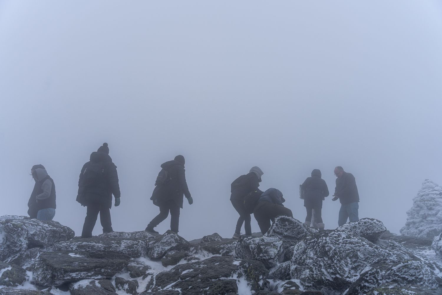 Group of hikers trekking through snowy, foggy mountain terrain in harsh winter conditions.
