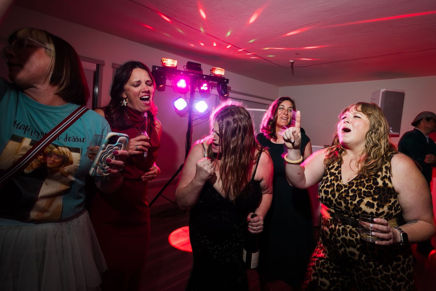 Women dancing and singing joyfully at a lively party with colorful stage lighting and a disco atmosphere.