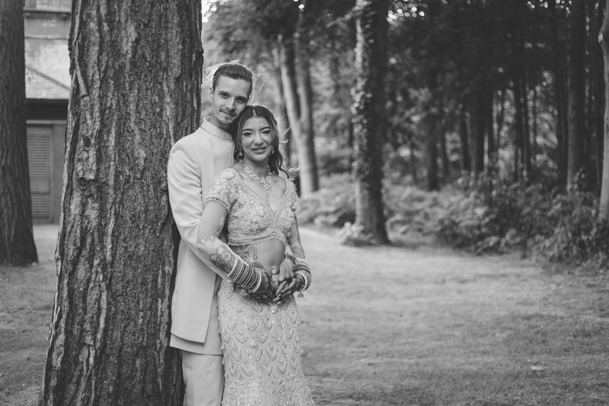 Black and white photo of a couple in wedding attire embracing by a tree at sunset at Pumping House wedding venue in Ollerton.
