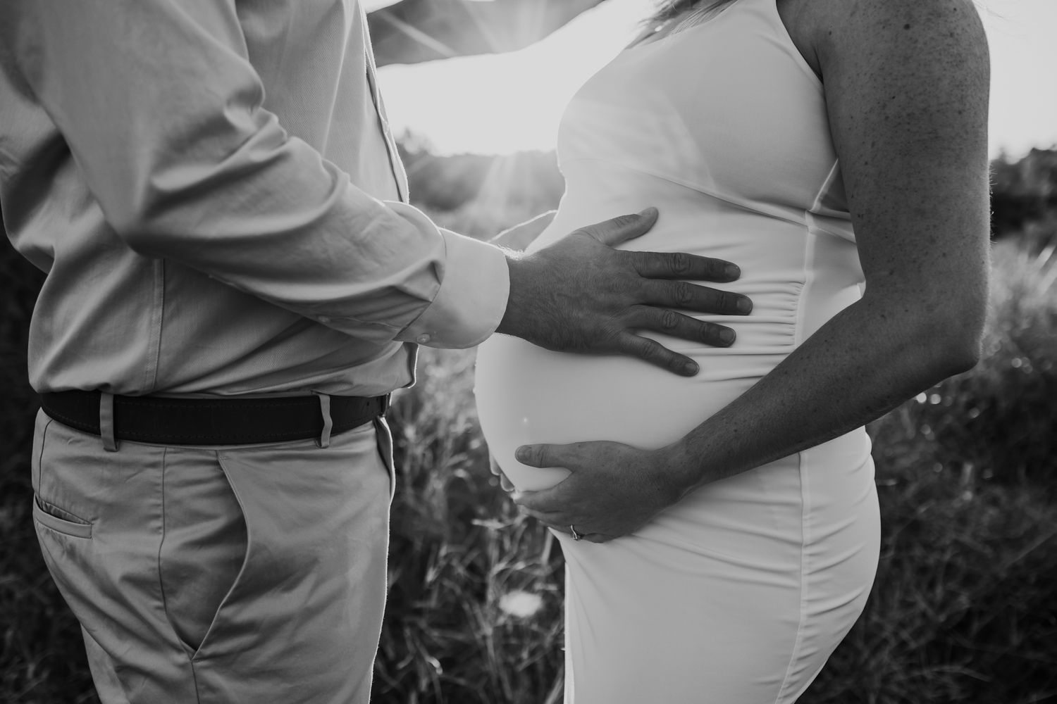 Black and white close-up of couple's hands on pregnant belly.