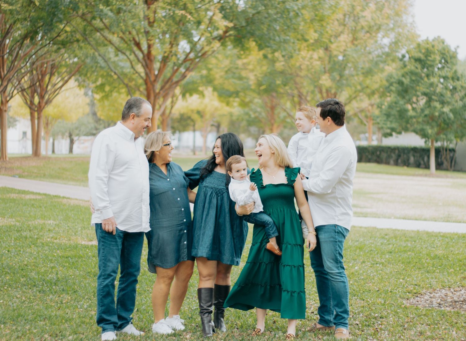 A group wearing coordinated green and white outfits stands together on grass under trees in a park setting.