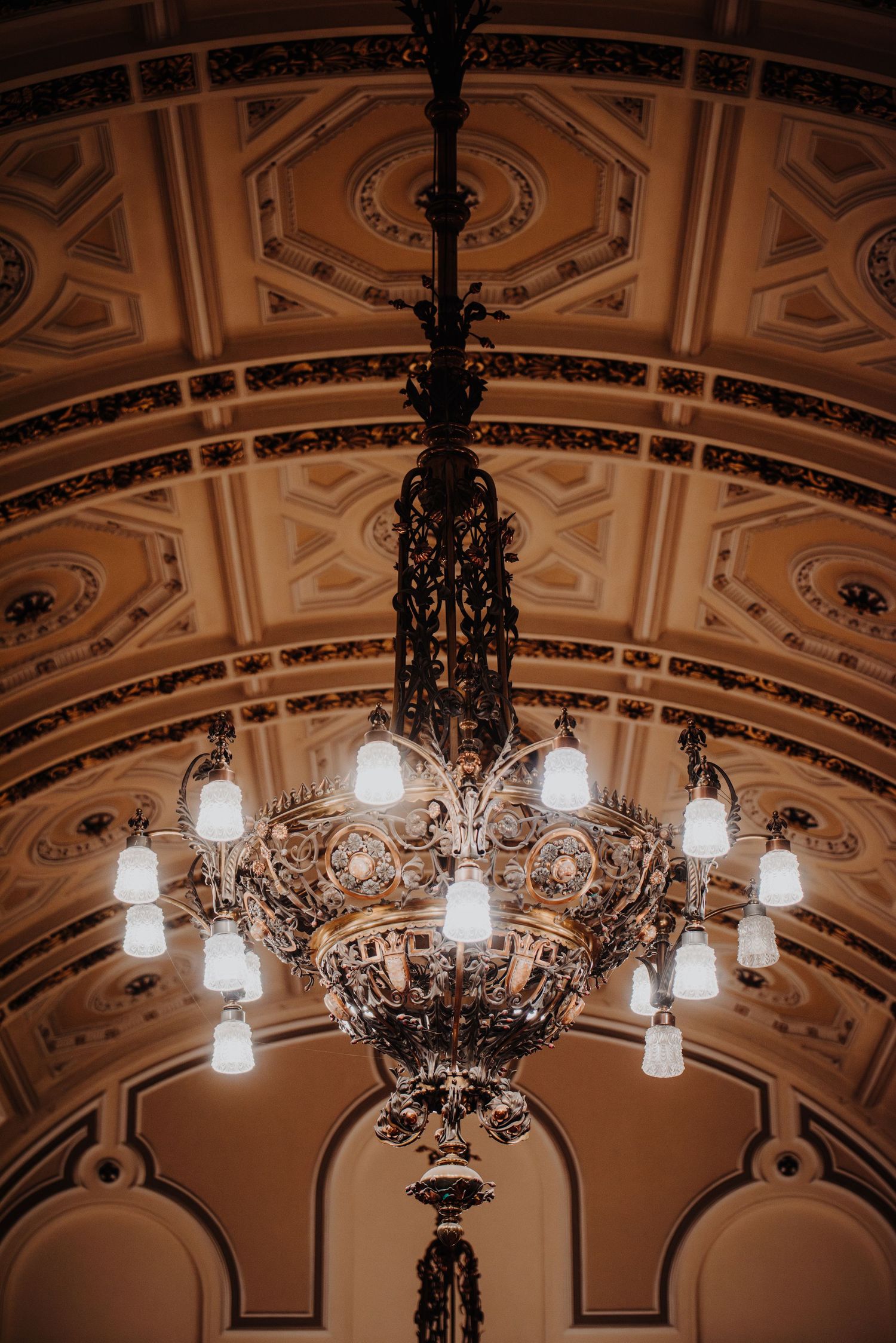 Ornate vintage chandelier with frosted glass lights illuminates decorated ceiling.