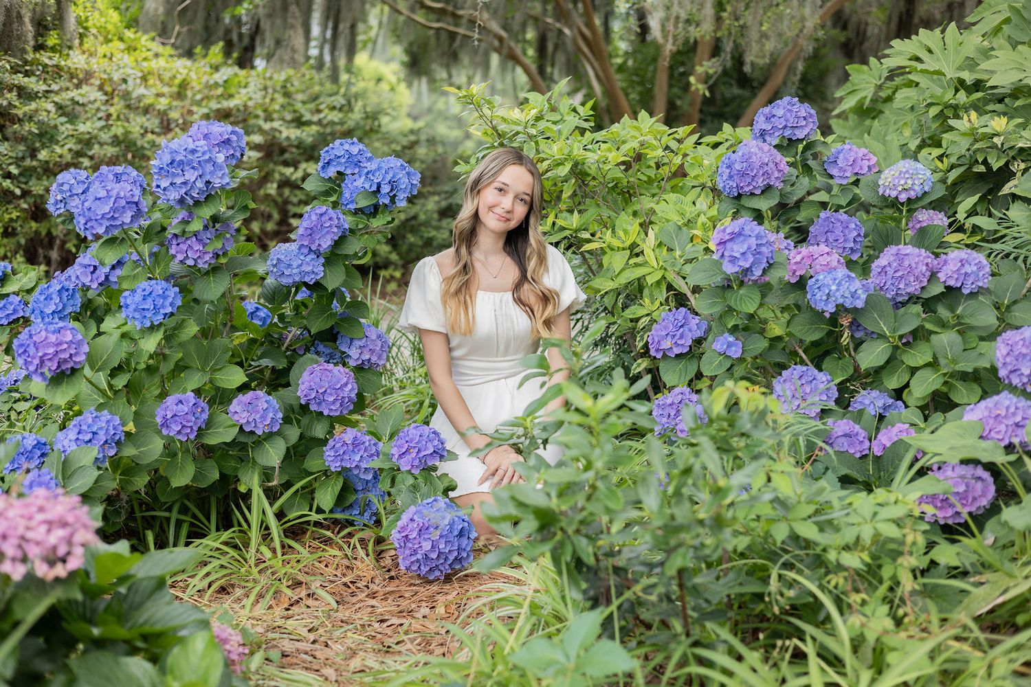 A white dress stands out among vibrant blue hydrangea blooms in a lush garden setting.
