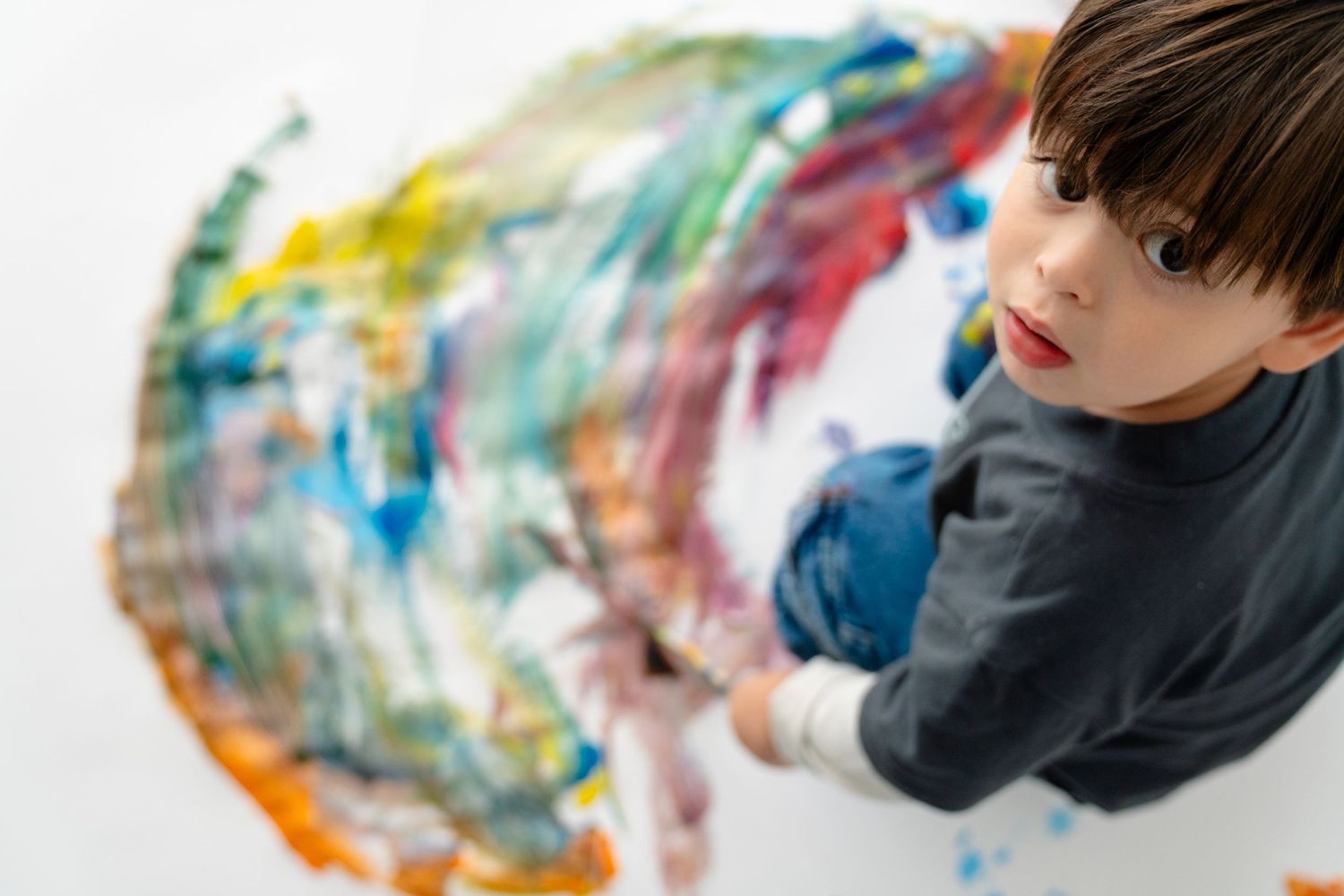 A young child's hands are seen creating colorful abstract art on a canvas.