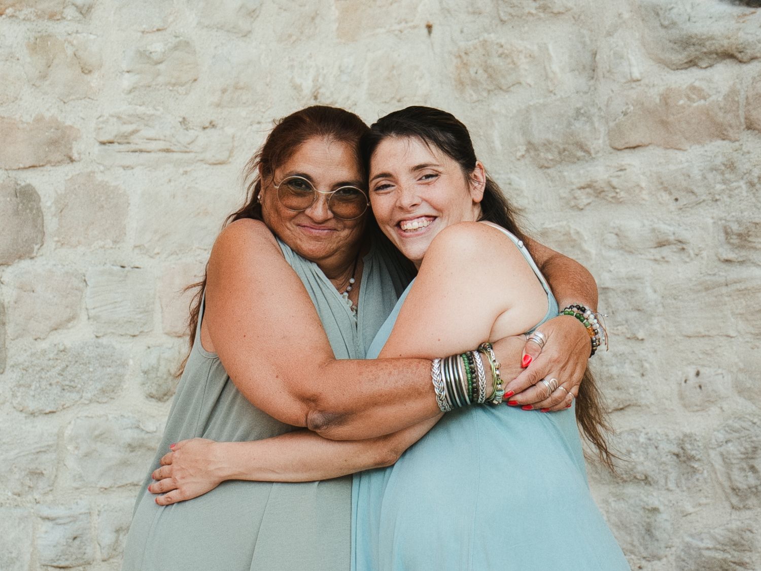 Une mère et sa fille adulte sourient, enlacées devant les pierres des remparts de Trets.