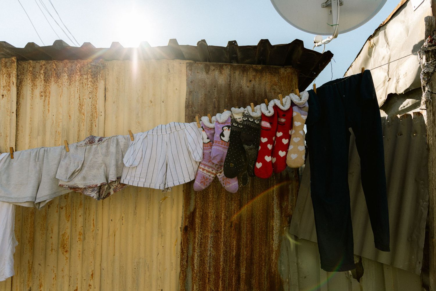 Colorful socks and clothes drying on a clothesline outside a rustic corrugated metal wall in sunlight.