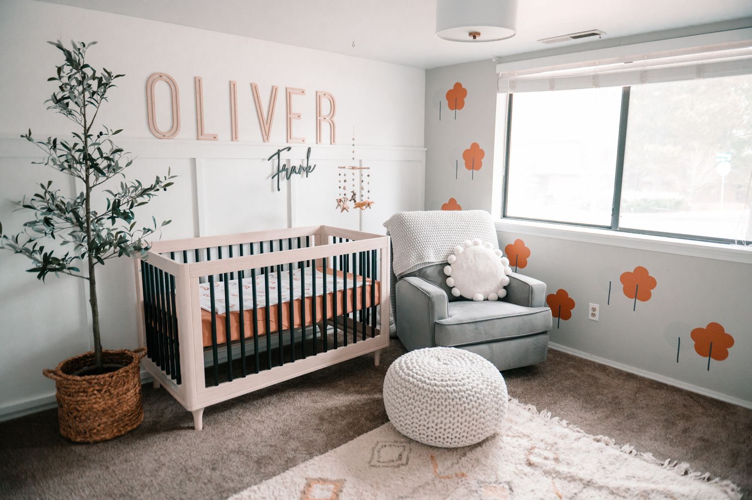 Modern nursery room with name Oliver on wall and minimalist white and orange decor.