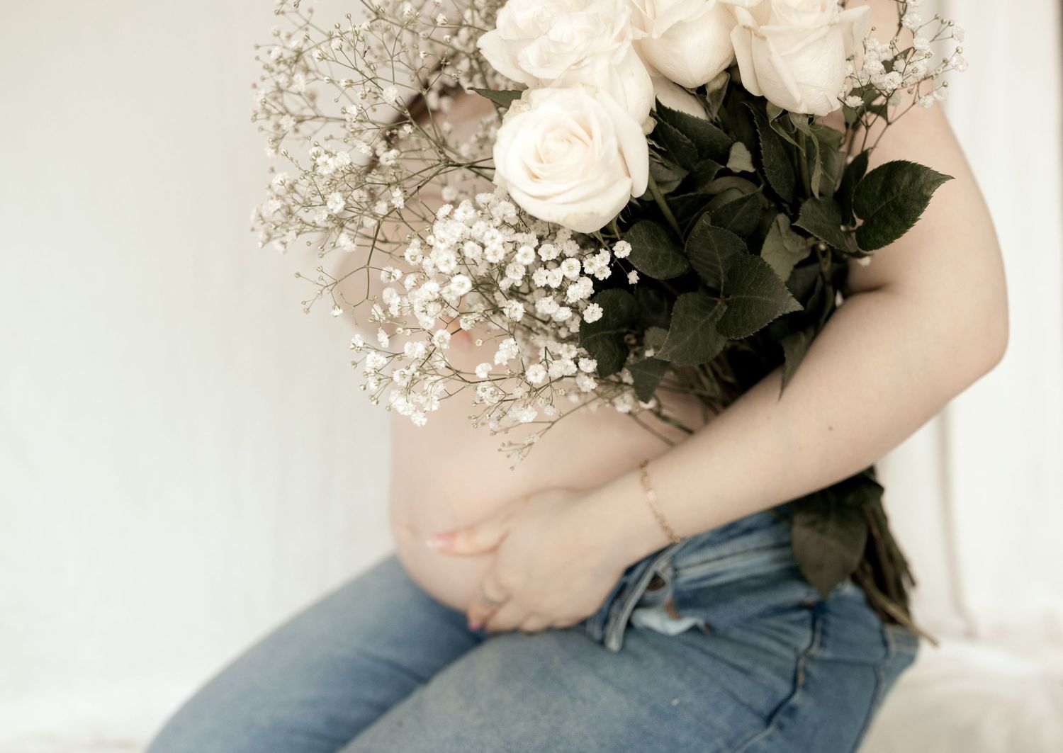 White roses and baby's breath bouquet held against denim jeans in soft natural light.