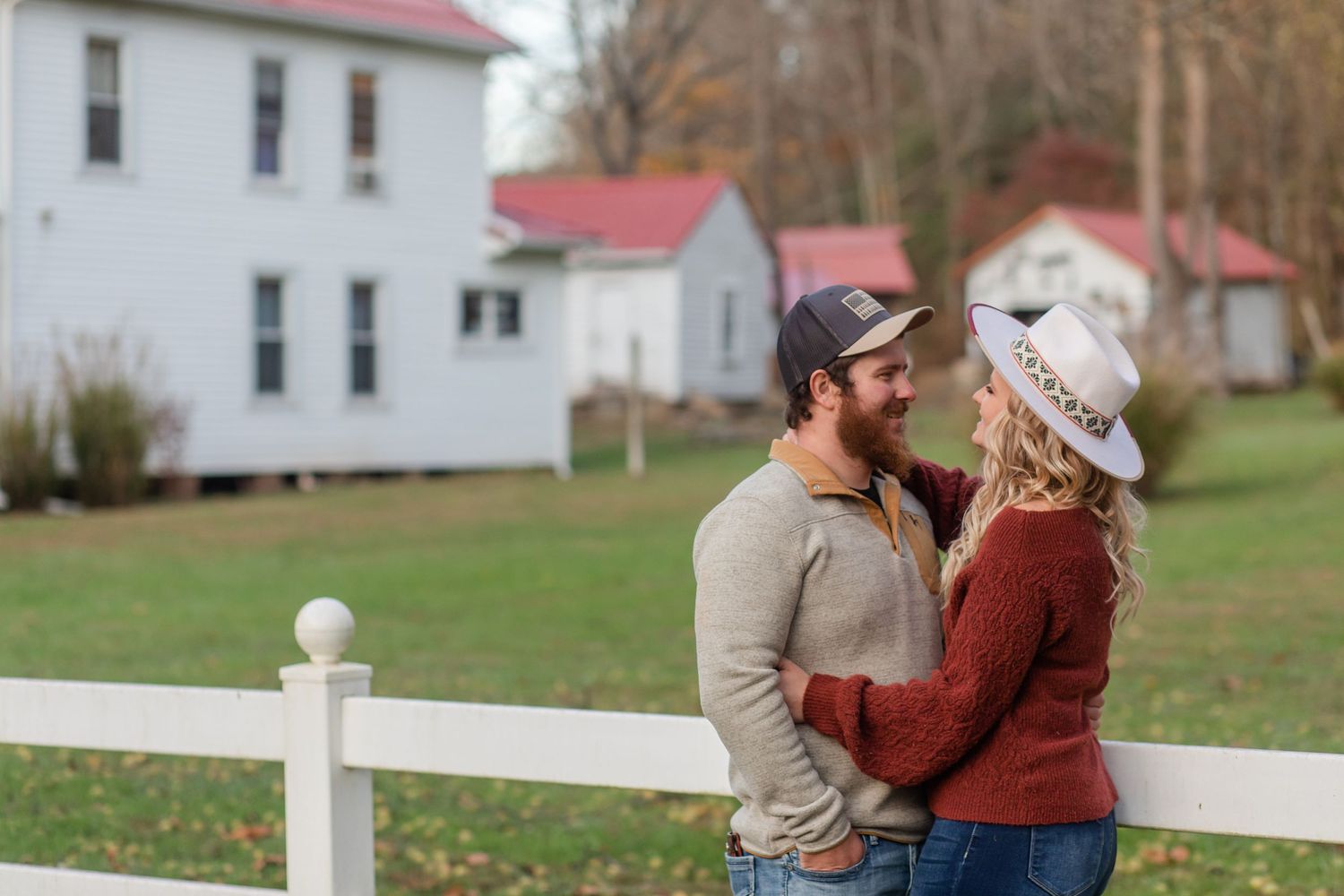 Couple walks hand in hand along a white fence on an autumn farm property.