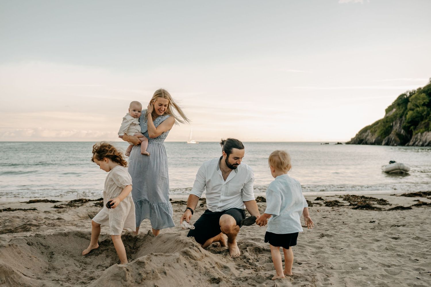 Family plays together on a scenic beach at sunset with rocky cliffs in the background.