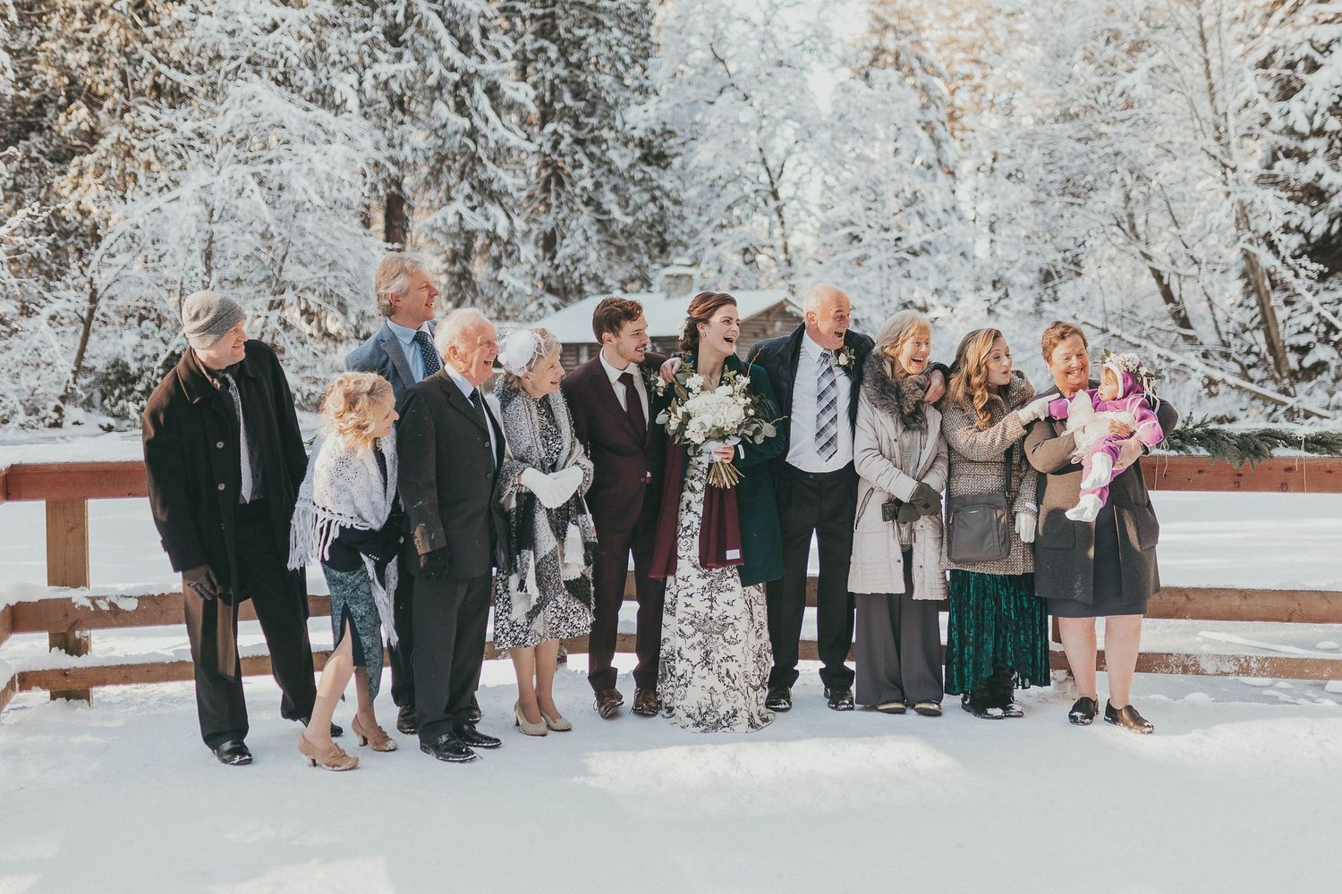 A large group gathered for a winter wedding photo in a snowy landscape.
