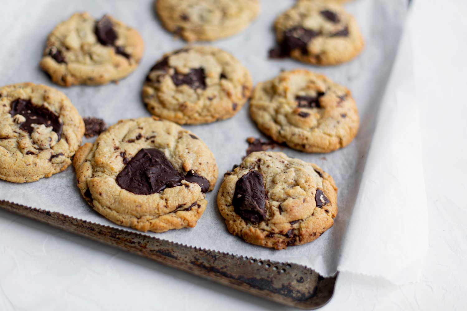 Freshly baked chocolate chip cookies cooling on dark baking sheet.