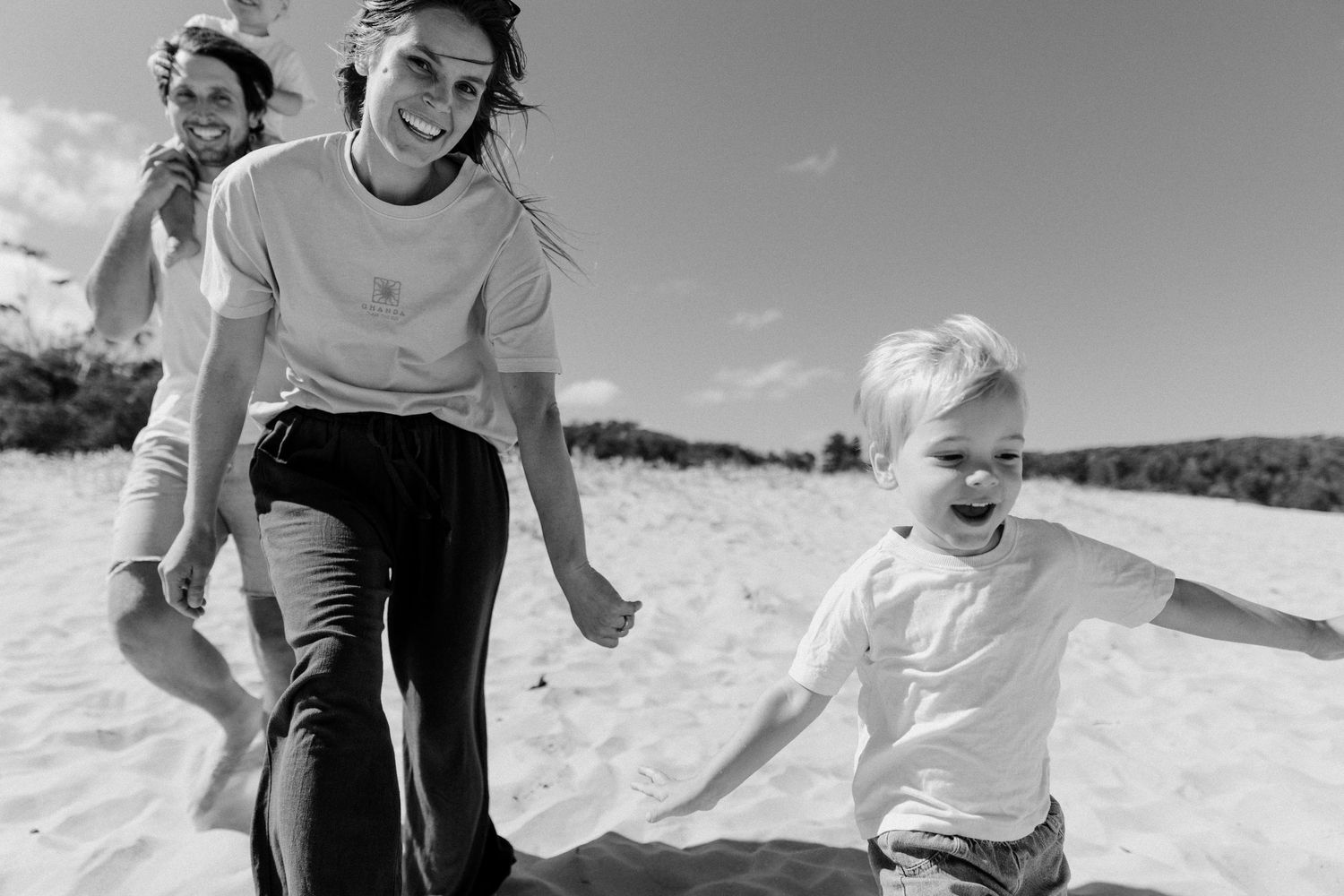 Black and white photo of a joyful family running on a sandy beach, with a laughing child spreading arms wide.