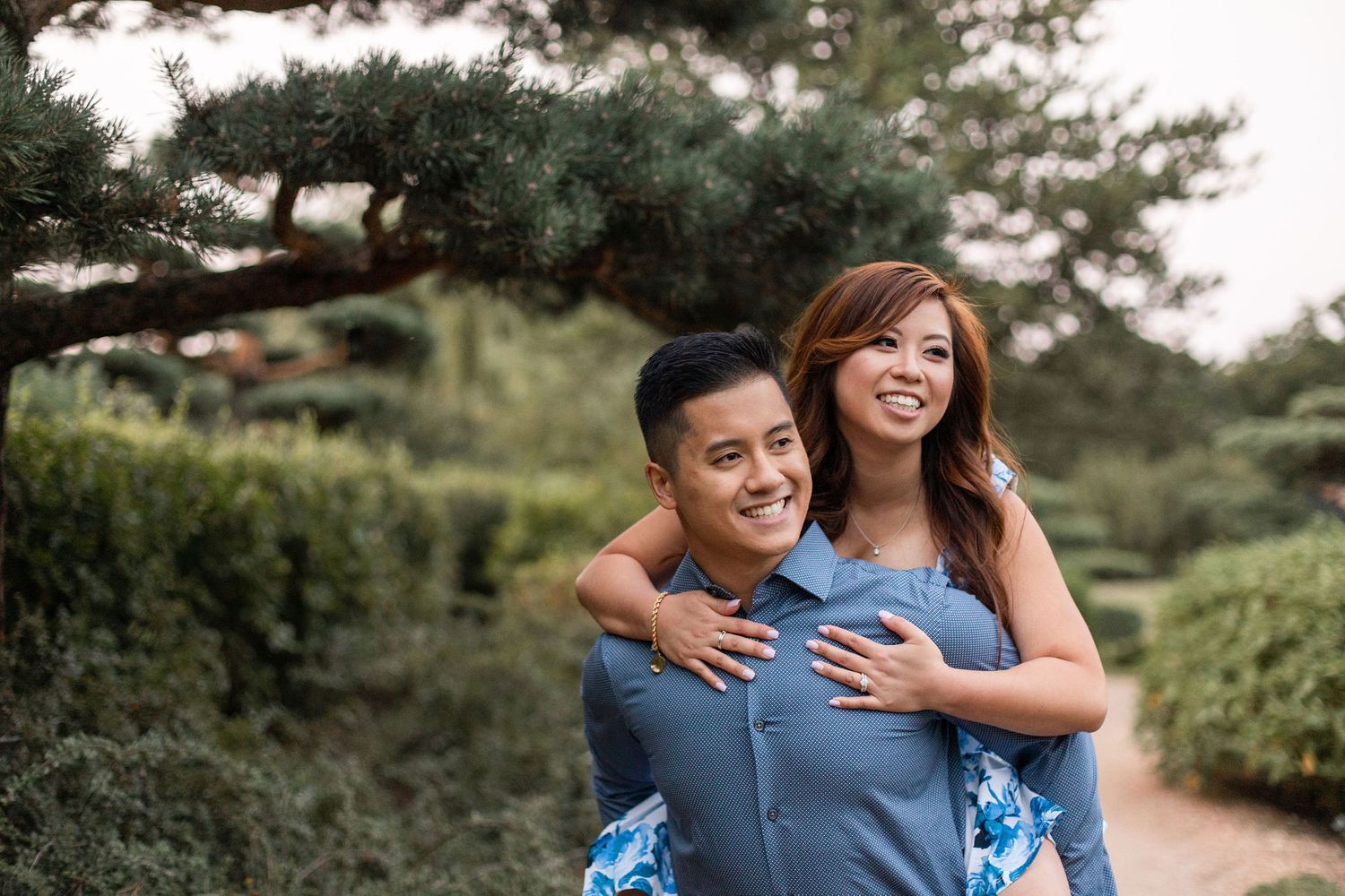 Couple in casual attire share a joyful moment outdoors with greenery in the background.