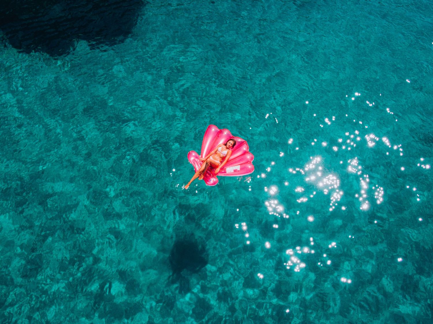 Pink inflatable float contrasting against turquoise Mediterranean waters viewed from above.