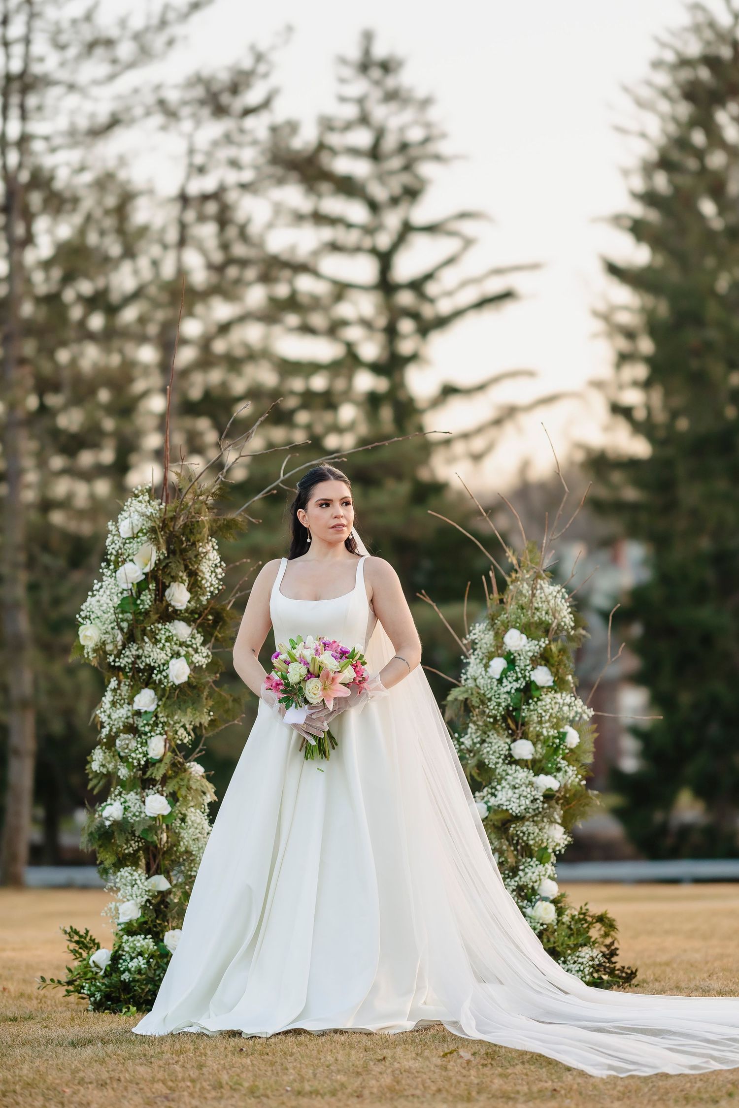 Elegant bridal portrait with white gown and floral arrangements in outdoor setting.
