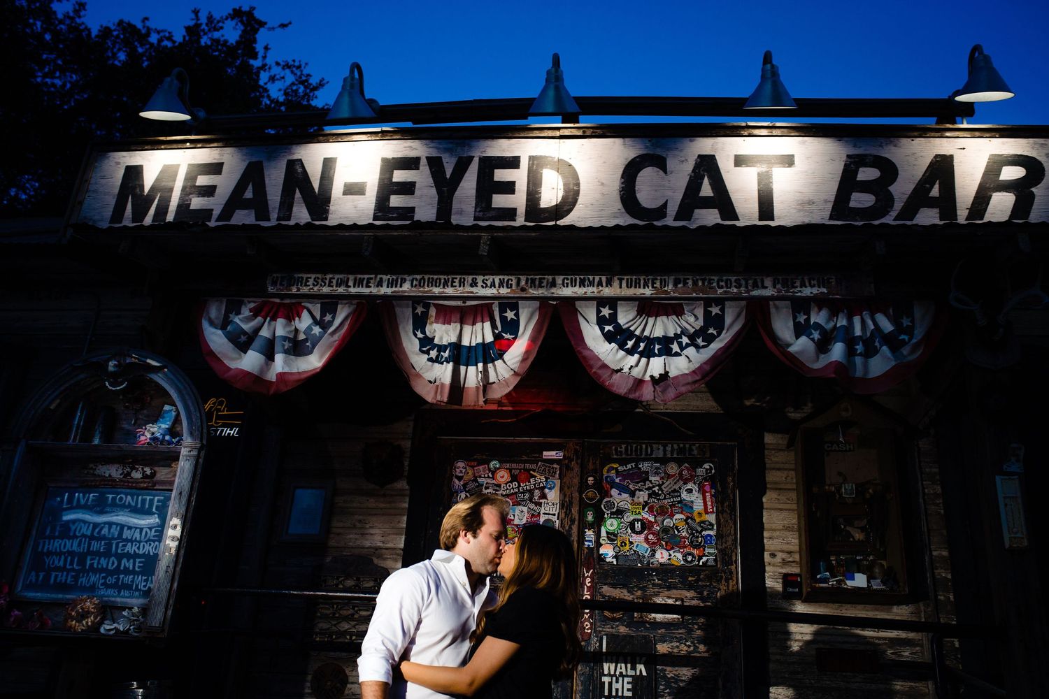 The illuminated Mean-Eyed Cat Bar sign with patriotic bunting decorations at night.