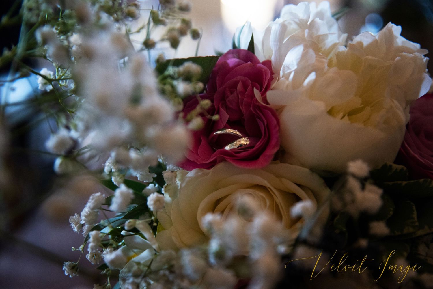 Soft focus arrangement of delicate pink and white flowers with green foliage in muted lighting.