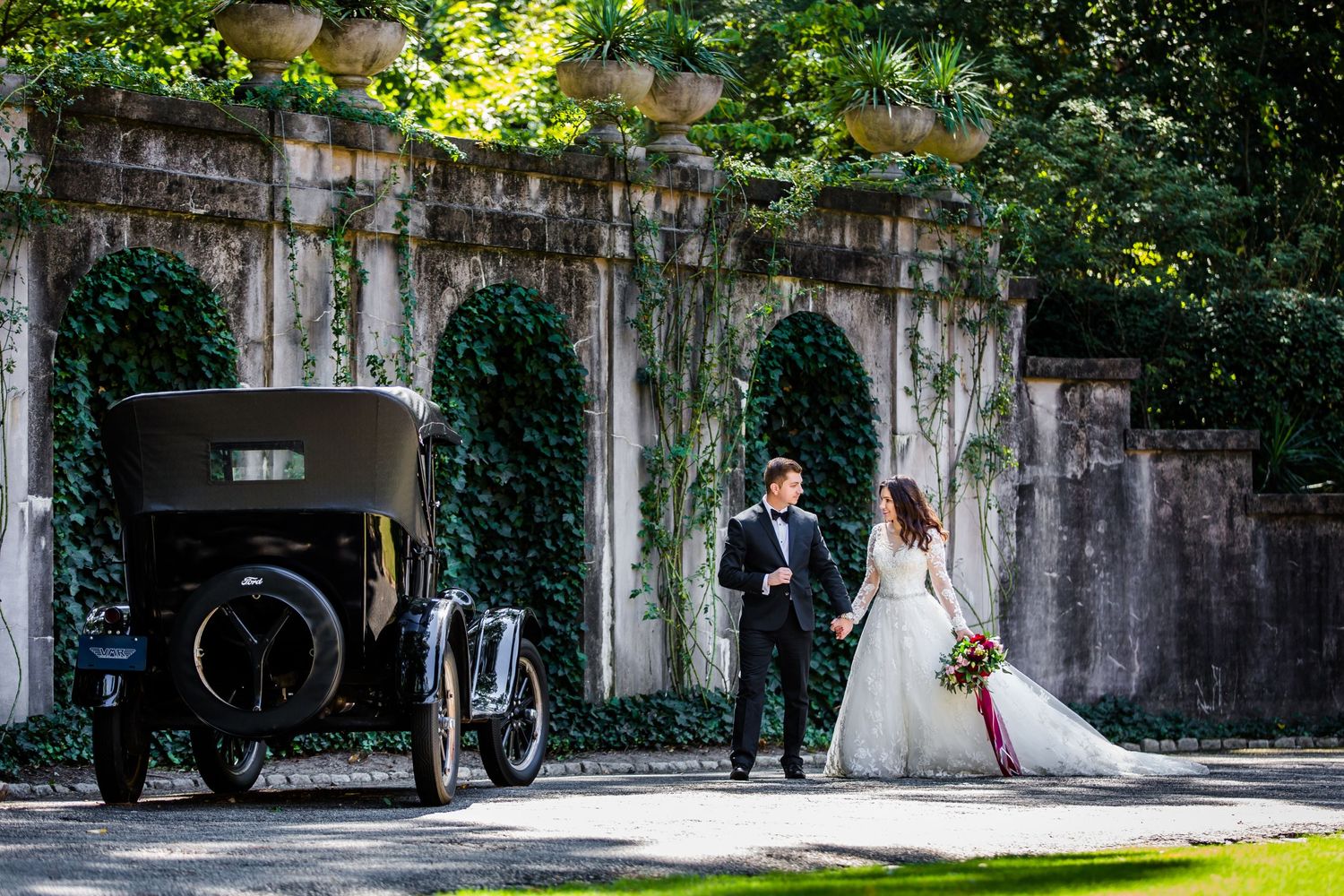 Vintage cars line a garden path during an outdoor wedding celebration.