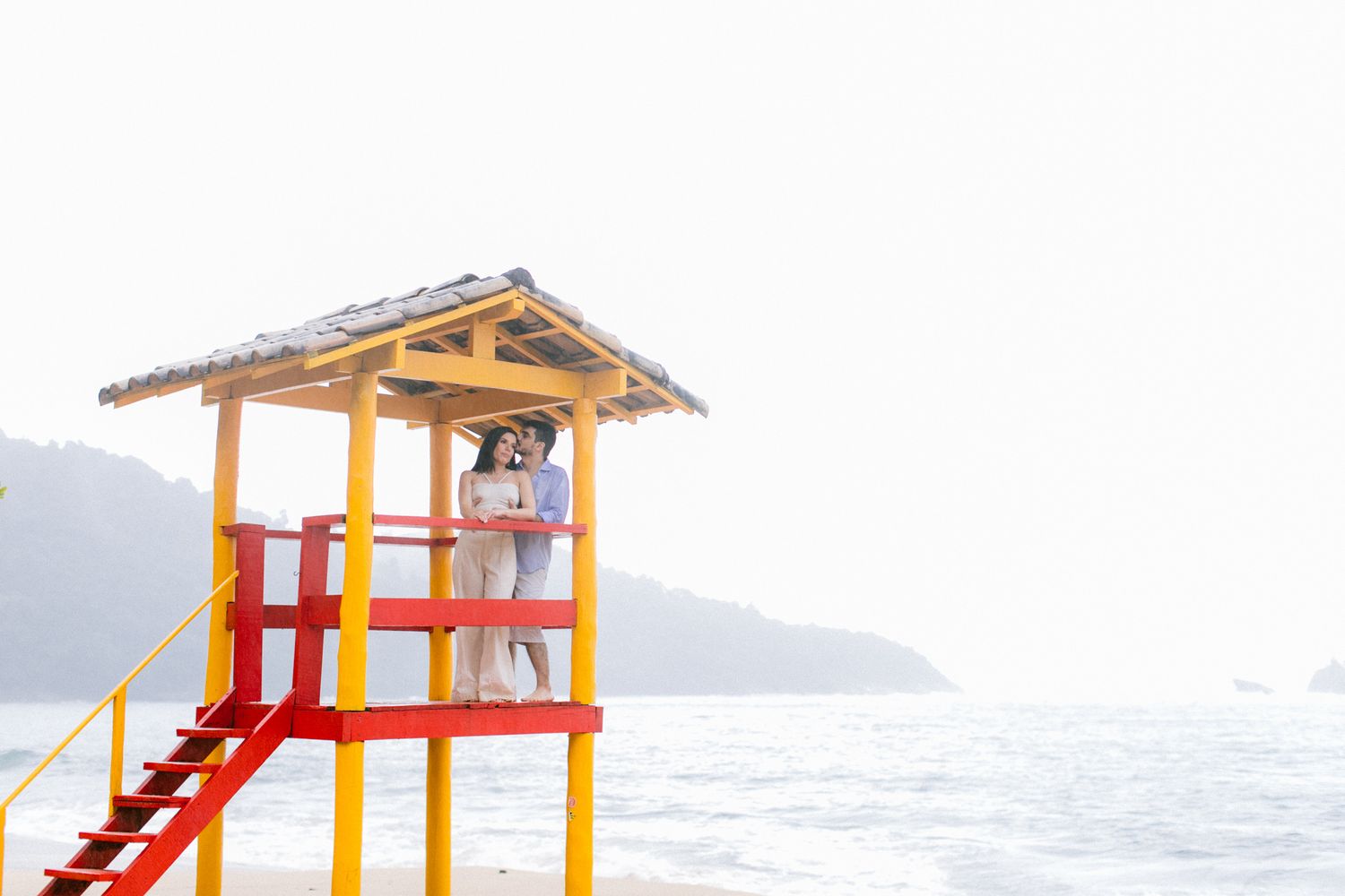 Colorful lifeguard tower with yellow and red details overlooking misty ocean view.