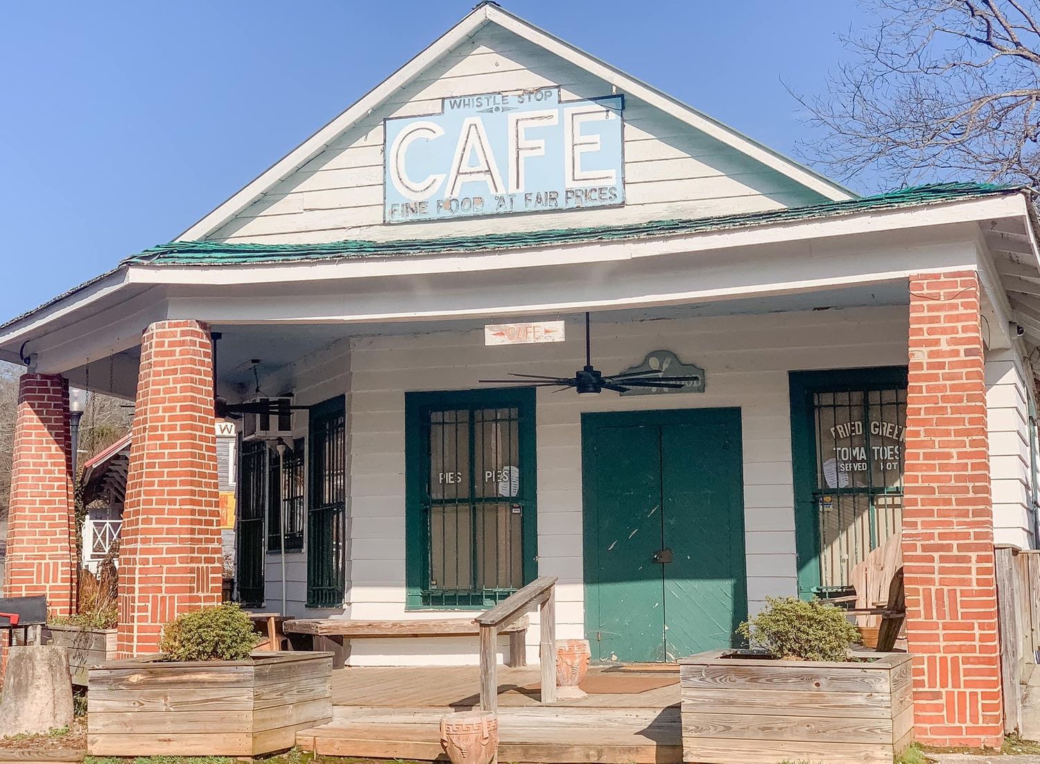 Row of vintage storefronts with brick columns and green trim in a historic district.