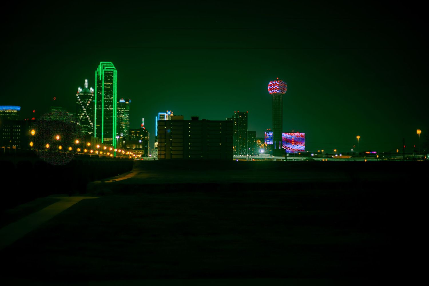 Green neon lights illuminate the Dallas skyline at night creating a dramatic urban landscape.