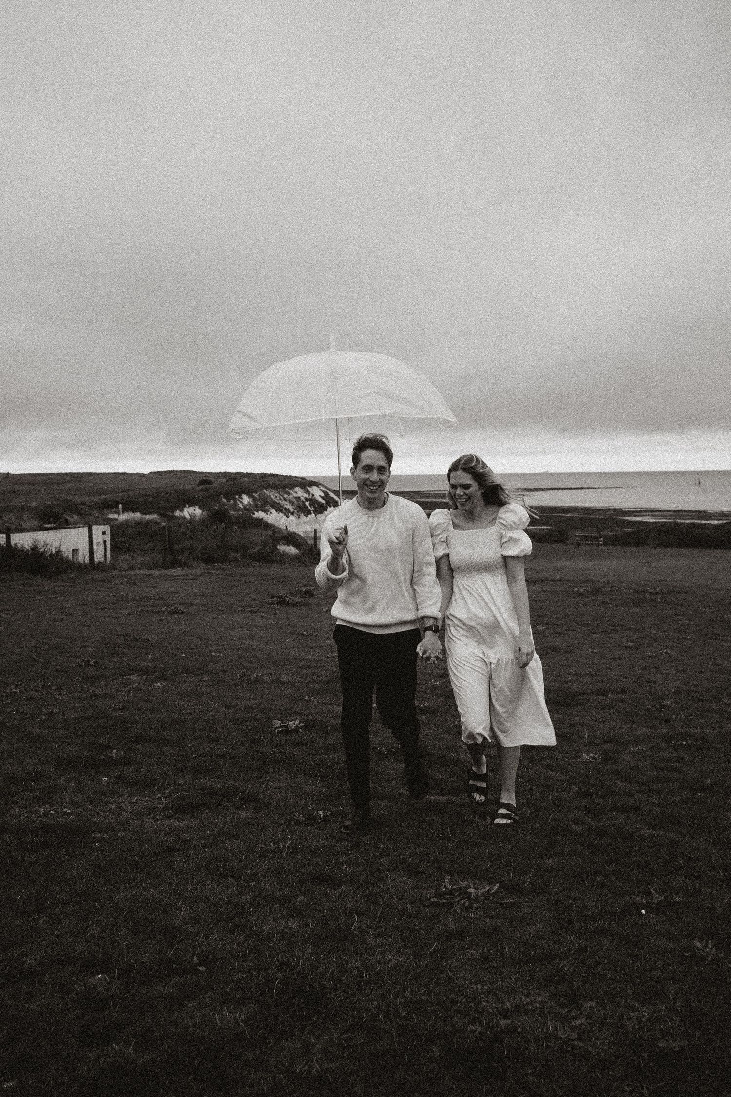 Couple walking with umbrella along coastal cliff in black and white.
