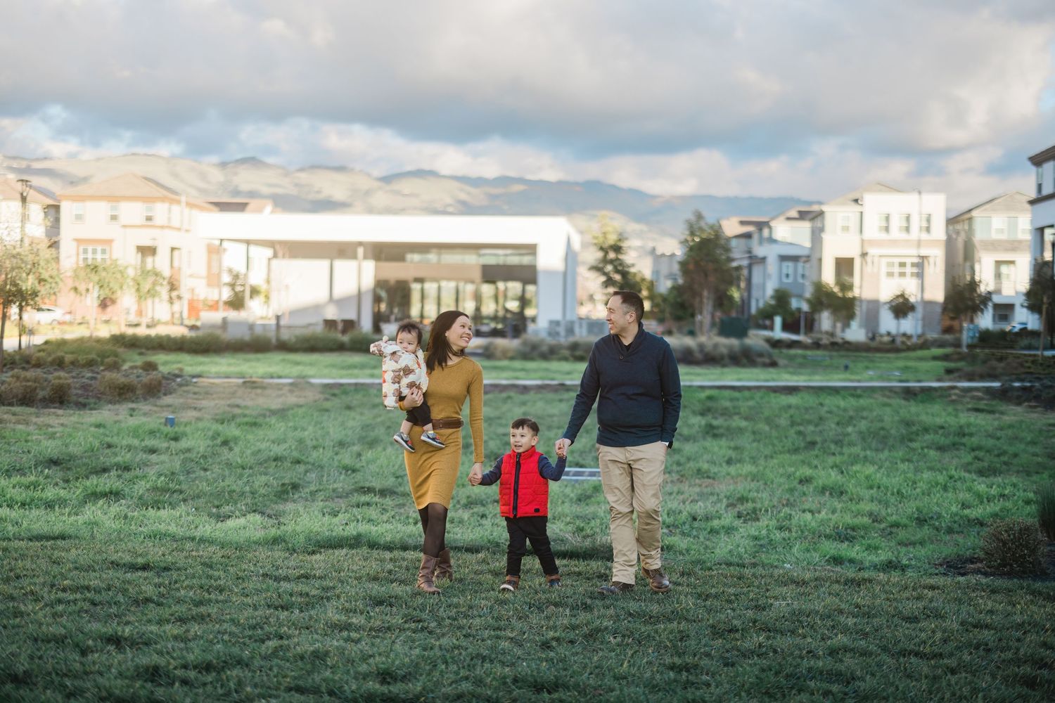 Family walking together across a green field with residential buildings in the background.