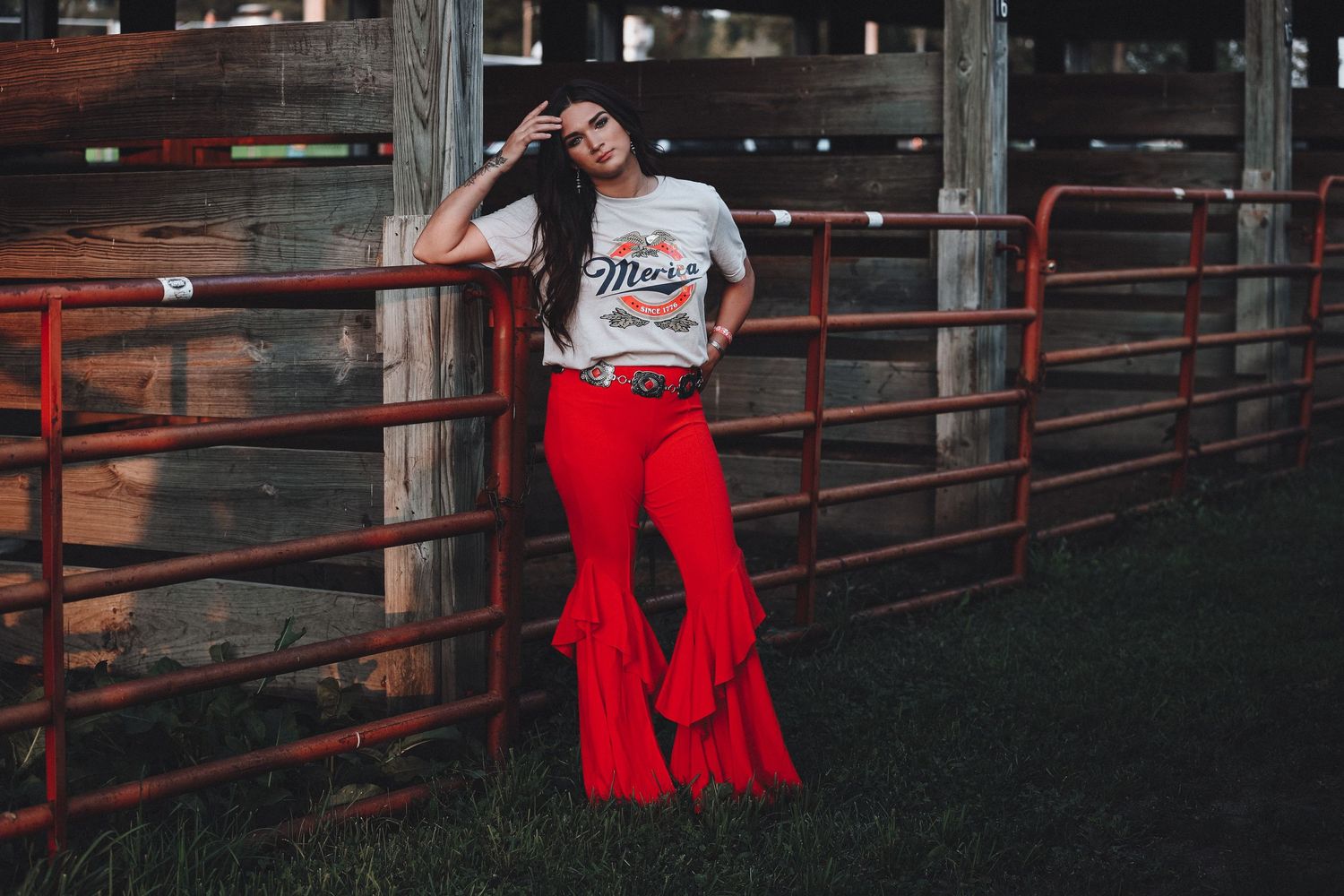 Western-style outfit with bright red bell bottoms and graphic tee near rodeo fence panels.
