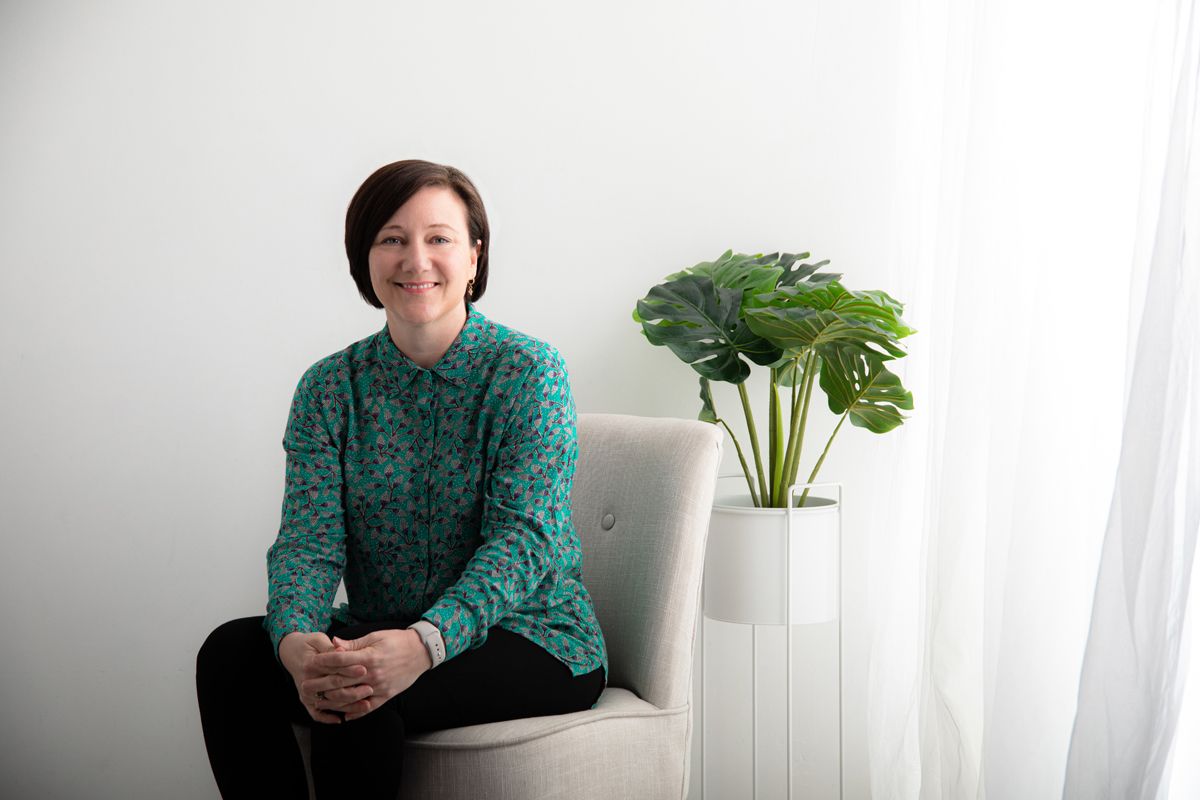 Person in green sweater sits beside modern white planter with monstera plant.