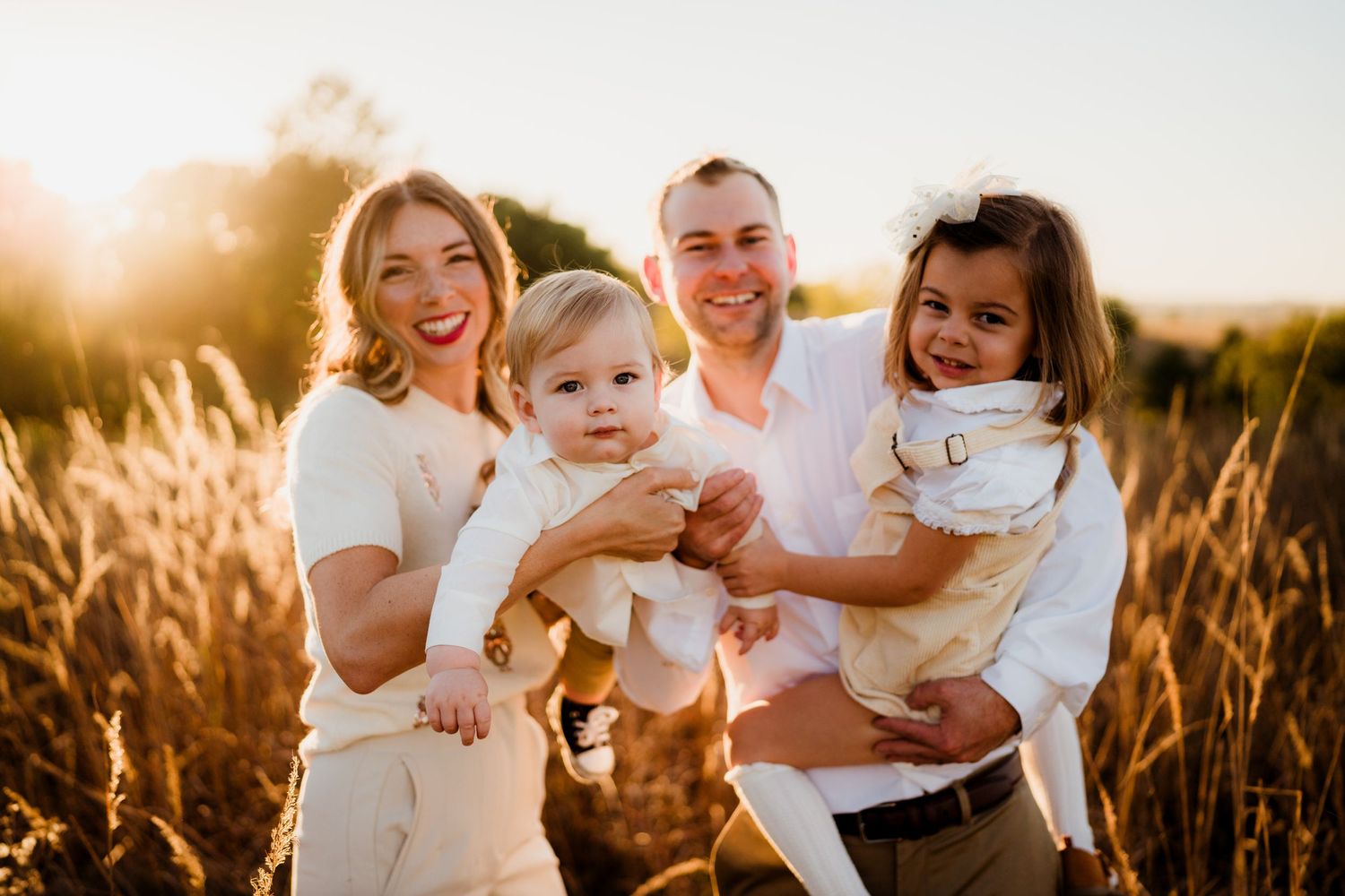 Family in white outfits posing together in a golden wheat field at sunset.