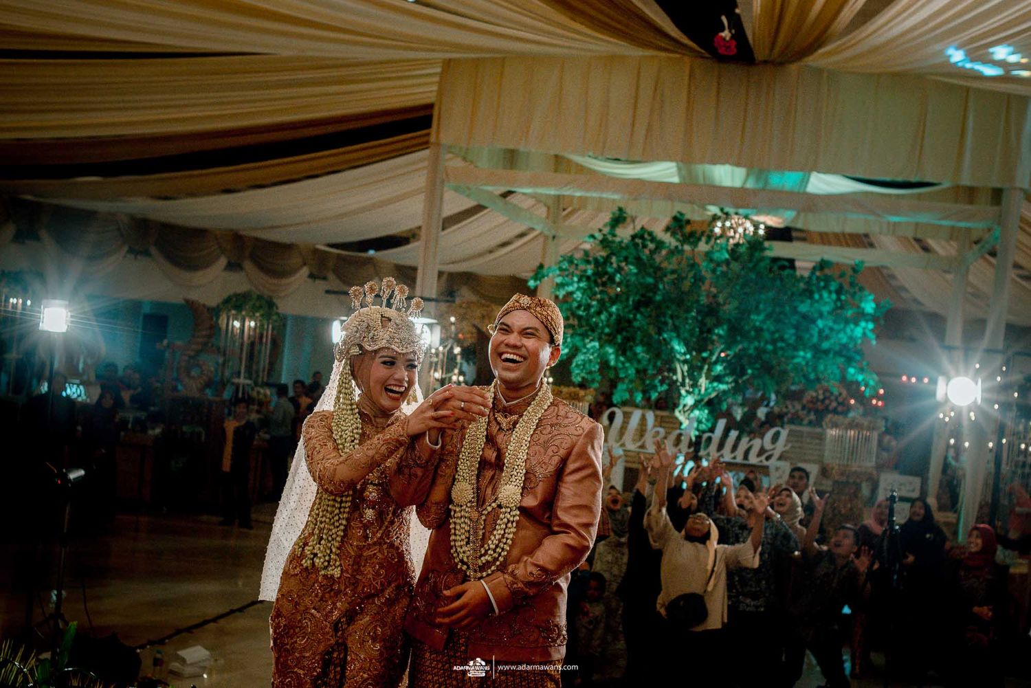 Traditional Indonesian wedding ceremony with couple in ornate attire under draped fabric decor.