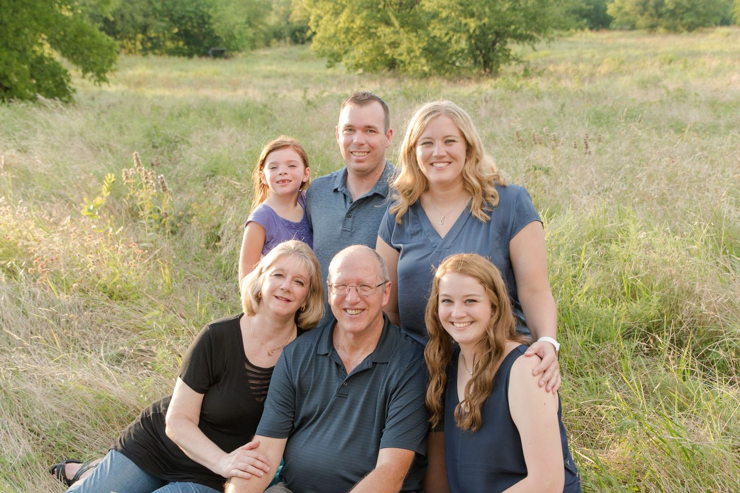 Multi-generational group posing together outdoors in tall grass field.