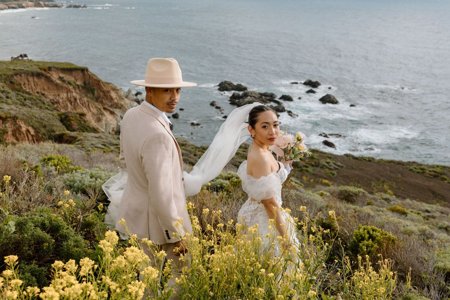 A coastal wedding photoshoot with wildflowers on a cliff overlooking the ocean.