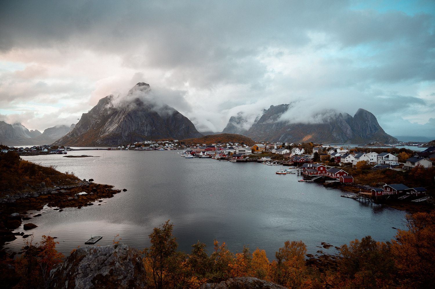 Scenic fjord landscape with traditional red houses nestled beneath misty mountains in Norway.