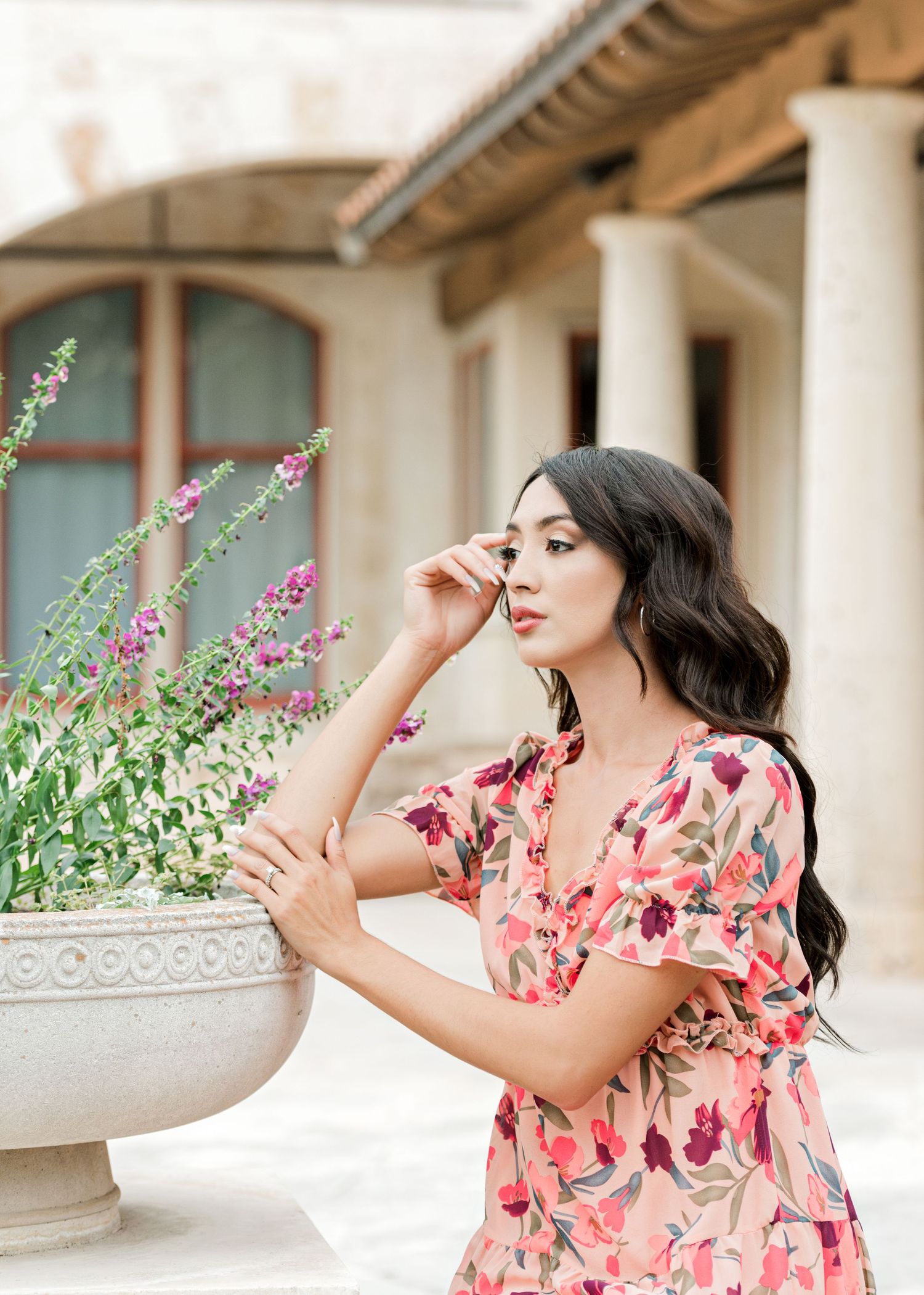 model in floral dress, sitting next to purple flowers, with her hand up by her face in Georgetown, TX