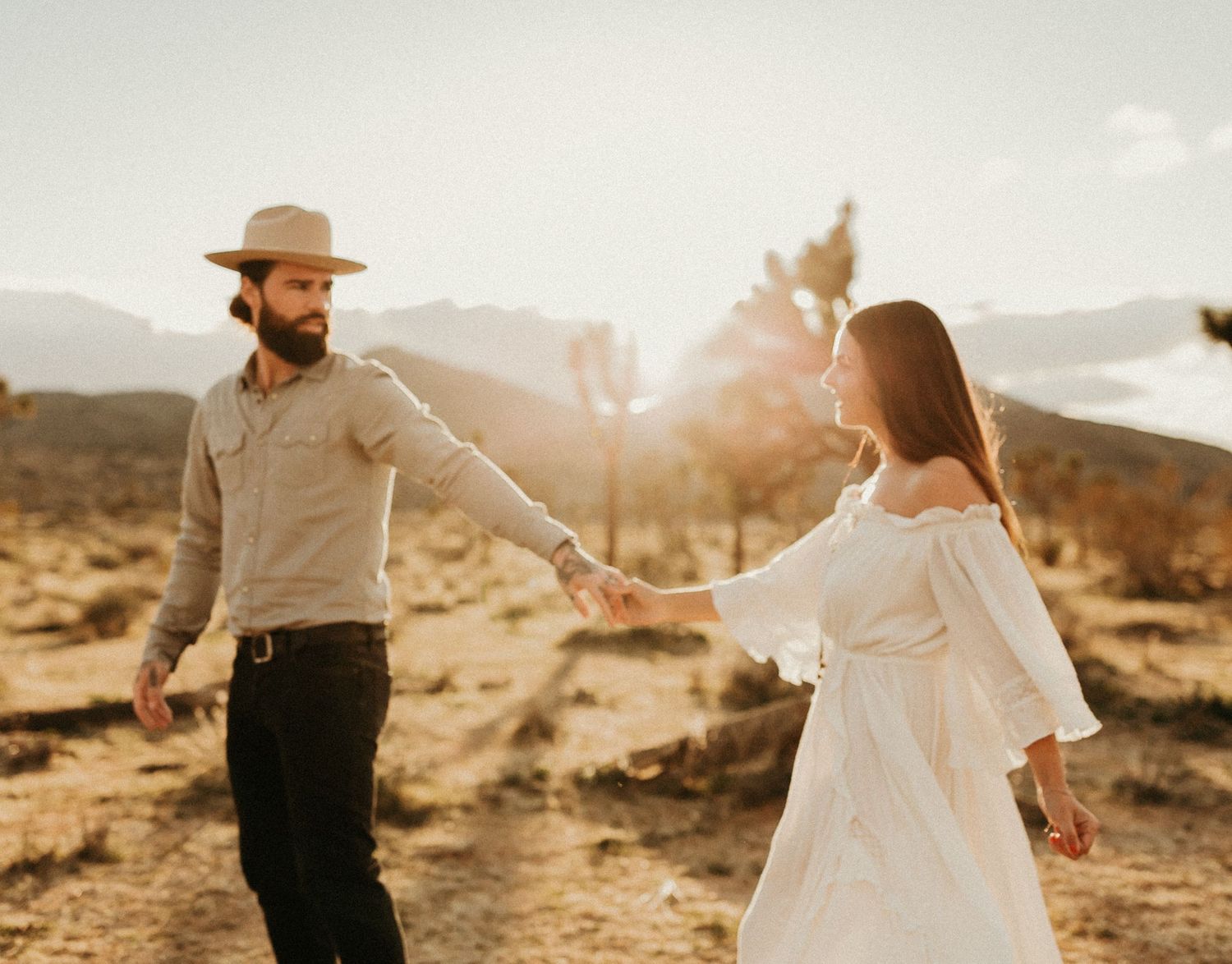 Couple holding hands in a desert landscape during golden hour.