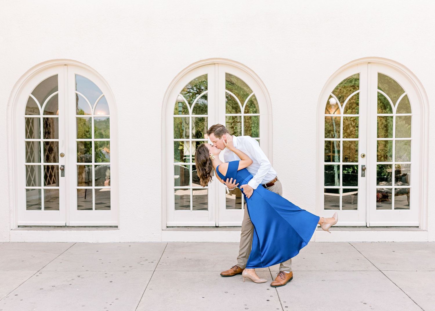 husband dipping his wife back as they kiss at Laguna Gloria in Austin, TX. her blue dress on full display.