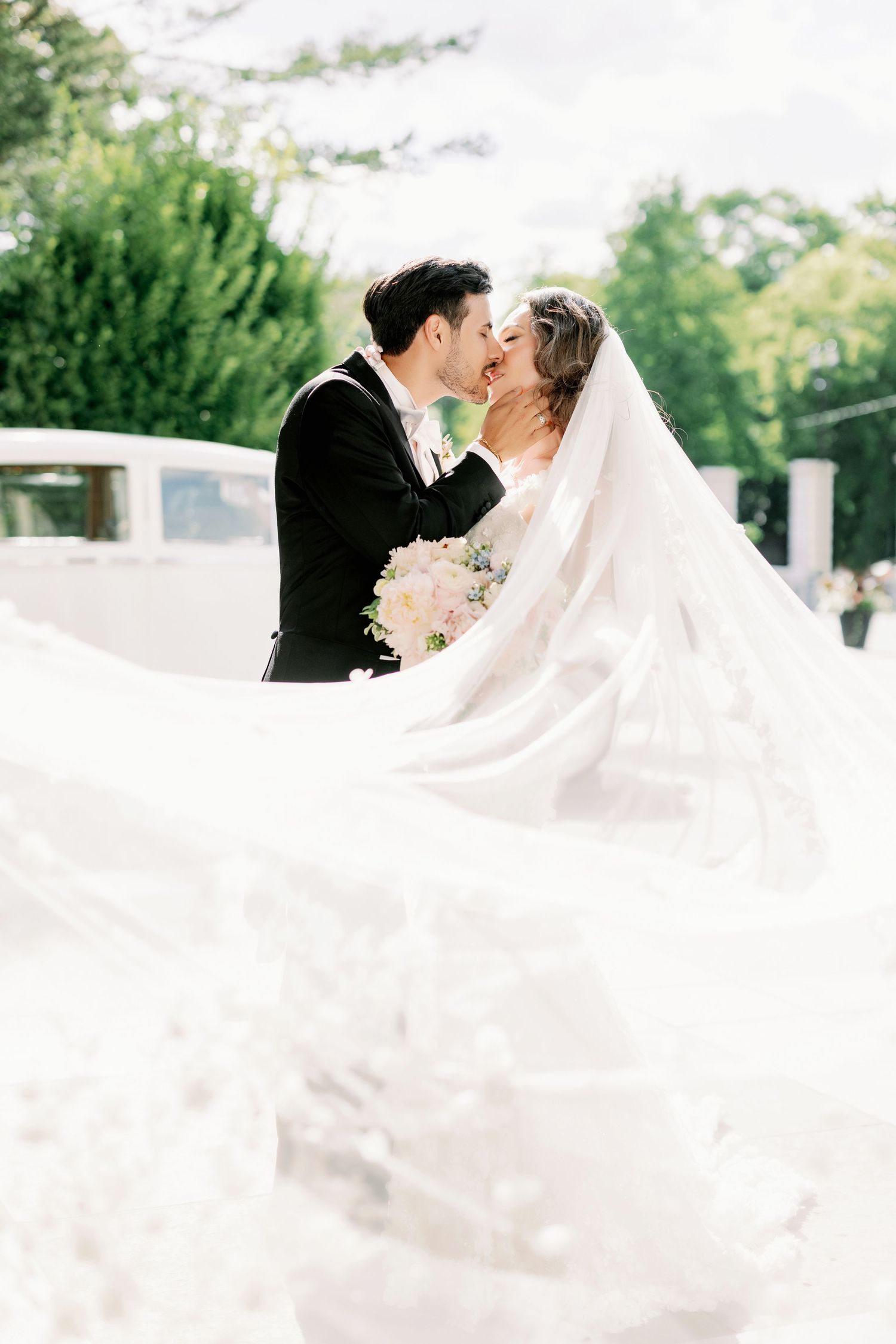 Romantic wedding portrait with flowing white veil caught in the breeze outdoors.