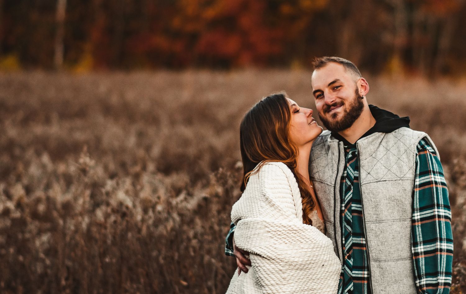 A romantic moment shared between two people in casual winter attire surrounded by autumn foliage.