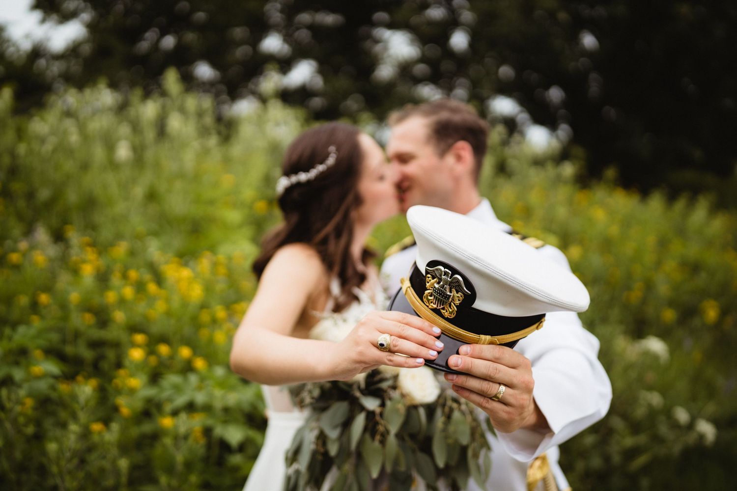A couple shares a romantic kiss in a field of yellow wildflowers while holding drinks.